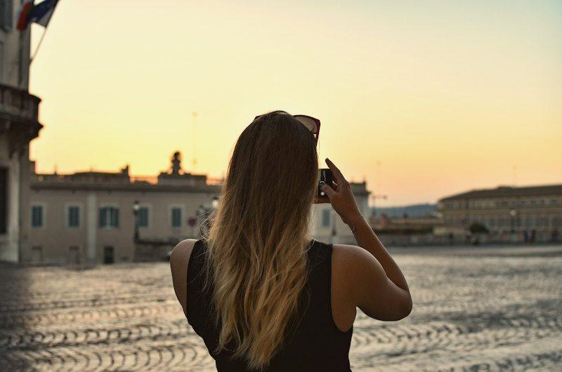 Mulher fotografando o pôr do sol numa praça